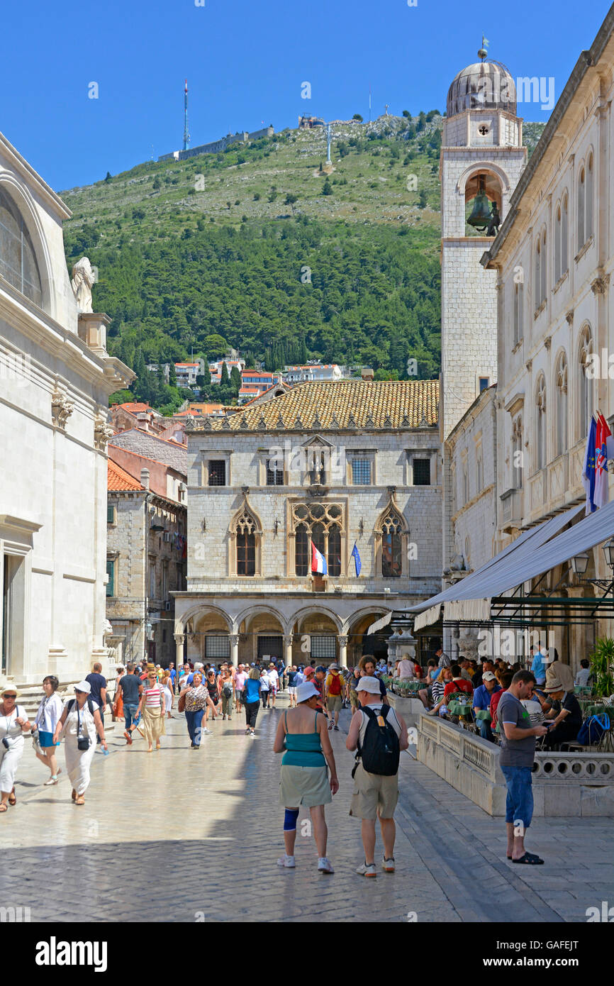 Straßenszene von Touristen in der Altstadt von Dubrovnik in Kroatien mit der Sponza-Palast und der Glockenturm in Luza Square blauer Himmel sonniger Tag Stockfoto