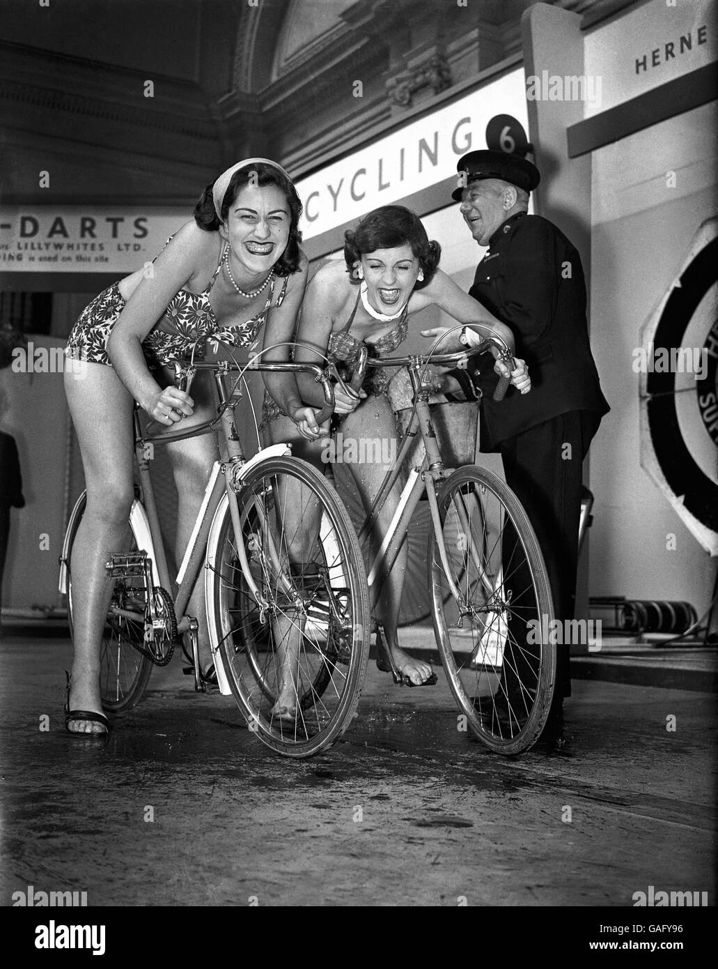 Zwei schwimmtaugliche junge Damen erhalten einen Schock einweichen von einem Der Angestellte, der die neuesten Raleigh-Fahrräder ausprobiert hat Stockfoto
