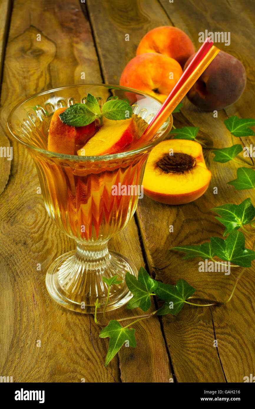Erfrischendes Getränk Eistee grüner Tee mit Pfirsichen und Minze in einem Glas auf einem dunklen Hintergrund aus Holz, vertikal, selektiven Fokus Stockfoto