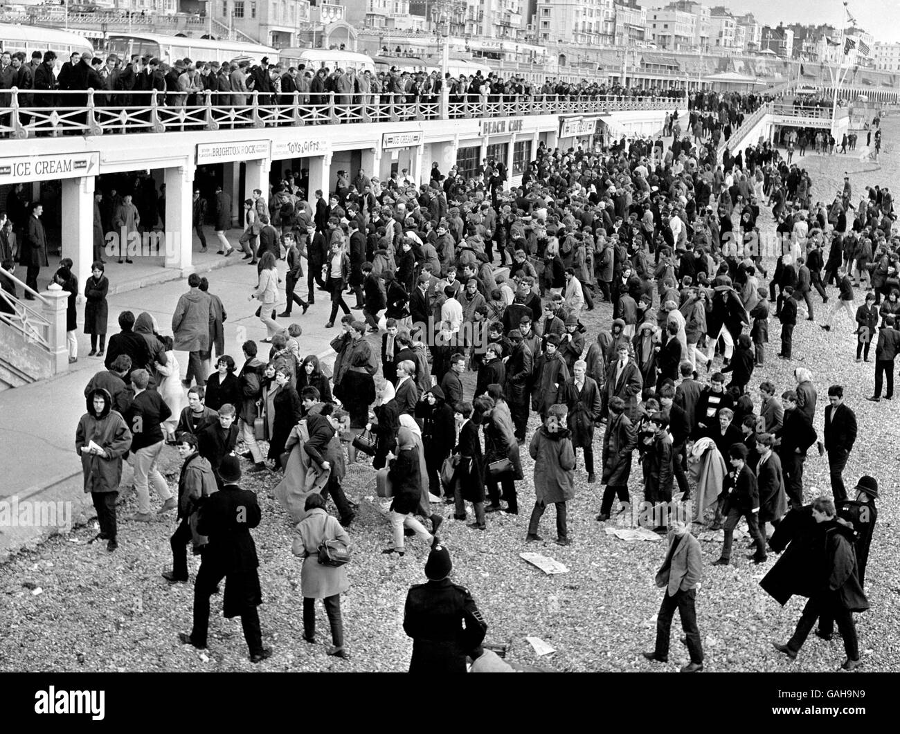 Interessierte Zuschauer beobachten vom Geländer der Promenade aus, wie die Polizei am Montag an den Feiertagen eine große Menge von Jugendlichen am Strand von Brighton hütete. Stockfoto