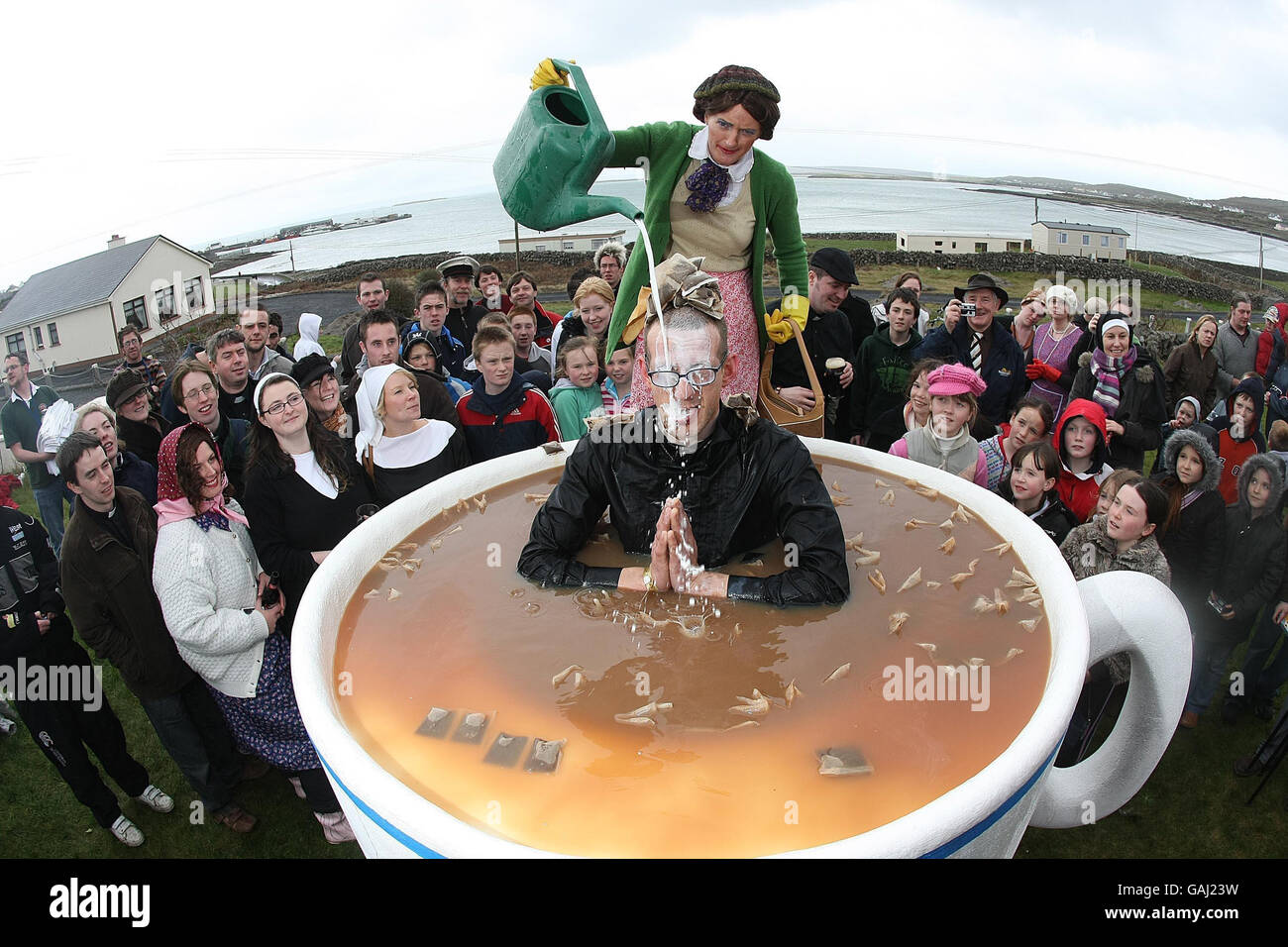 Pater Ted Fan Peran Odges sitzt in einer riesigen Tasse Tee, während Frau Doyle während des Father Ted Festivals auf den Aran-Inseln Milch über ihn gießt. Stockfoto