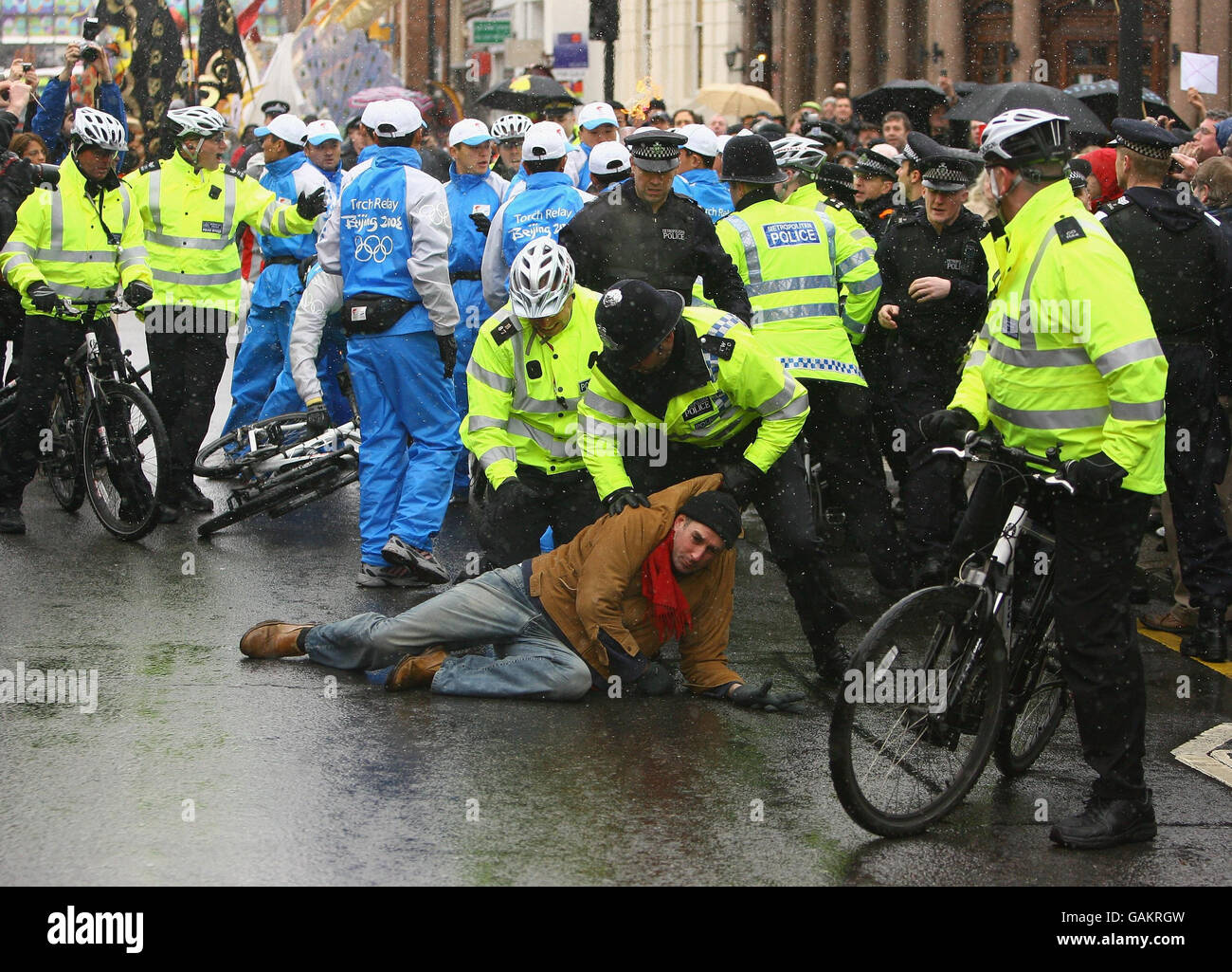 Ein Polizist ringt einen Demonstranten zu Boden, nachdem er während eines Teils seiner Reise durch London die olympische Fackel von der britischen Fernsehmoderatorin Konnie Huq (nicht gesehen) auf dem Weg zur Beleuchtung des olympischen Kessels in der O2 Arena in Greenwich gepackt und versucht hat, sie mit sich zu nehmen. Stockfoto