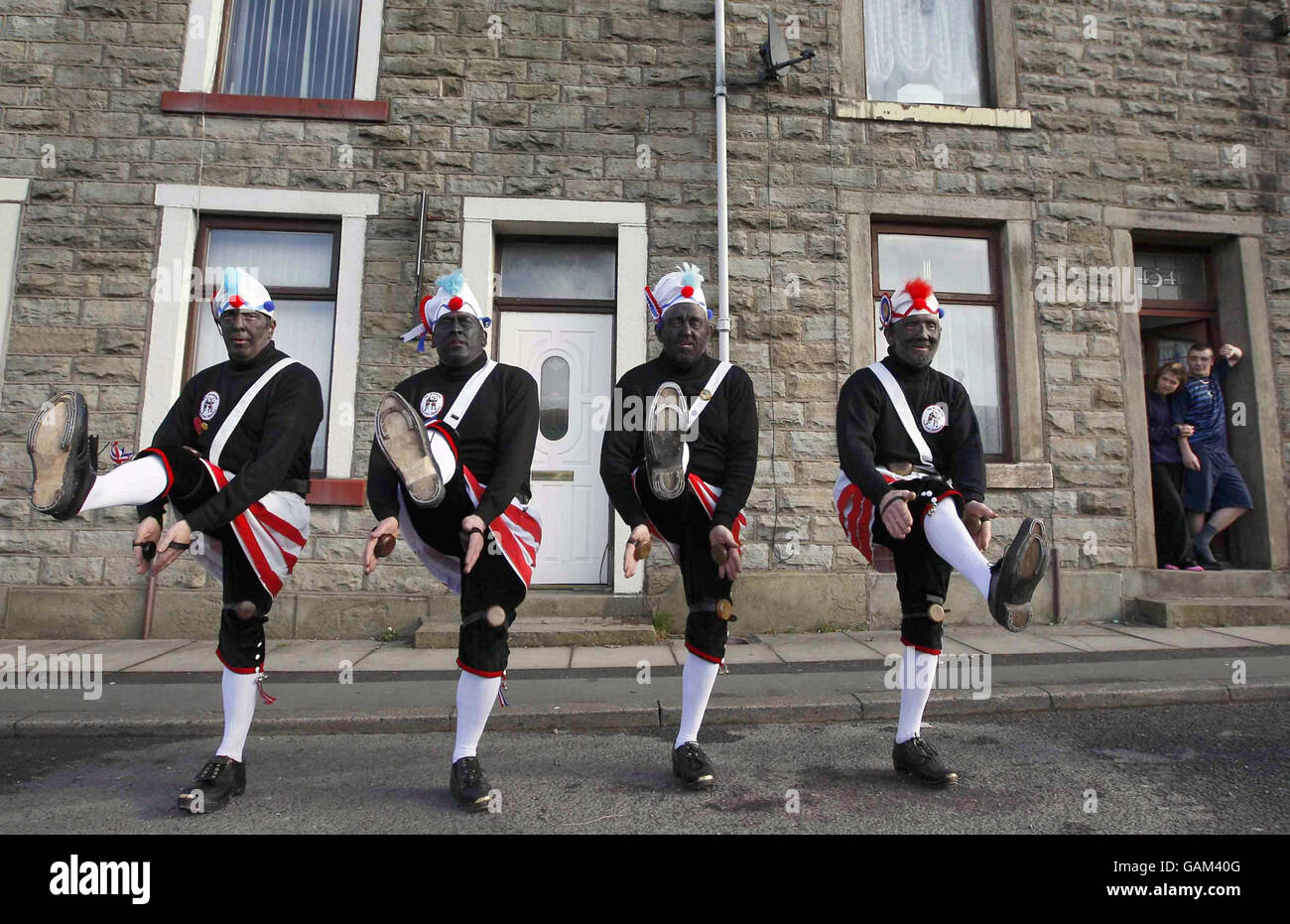 Mitglieder der Britannia Coconut Dancers of Bacup auf den Straßen in der Nähe von Bacup während ihres traditionellen jährlichen Ostersamstags-Tanzes. Es wird angenommen, dass die geschwärzten Gesichter einen heidnischen oder mittelalterlichen Hintergrund widerspiegeln könnten, als es getan wurde, um die Tänzer vor bösen Geistern zu verbergen. Alternativ kann es einen Bergbau-Hintergrund widerspiegeln. Stockfoto