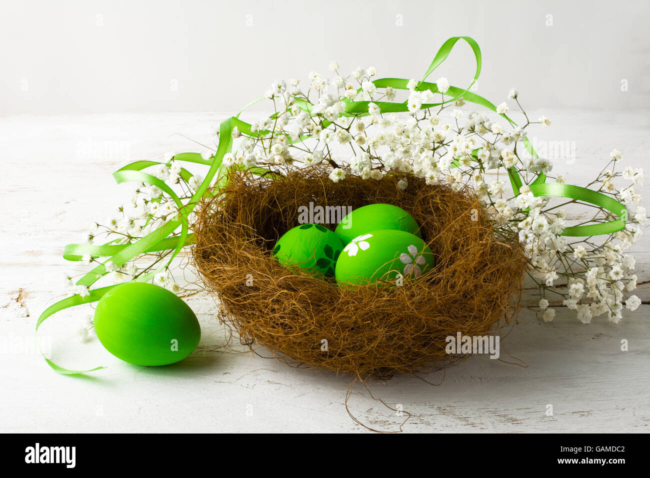 Grüne Ostereier in einem Nest mit grünem Satinband auf einem weißen Hintergrund Holz Stockfoto