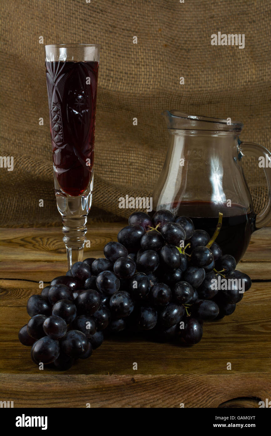 Dunkle Traube und einem Glas Wein auf einem dunklen Hintergrund aus Holz. Haufen von Trauben. Cluster-Trauben.  Bündel Weintrauben. Trauben. Gr Stockfoto