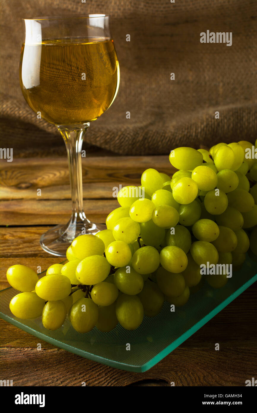 Weiße Trauben und einem Glas Wein auf einem dunklen Hintergrund aus Holz. Cluster von Trauben. Haufen von Trauben. Cluster-Trauben.  Bunc Stockfoto