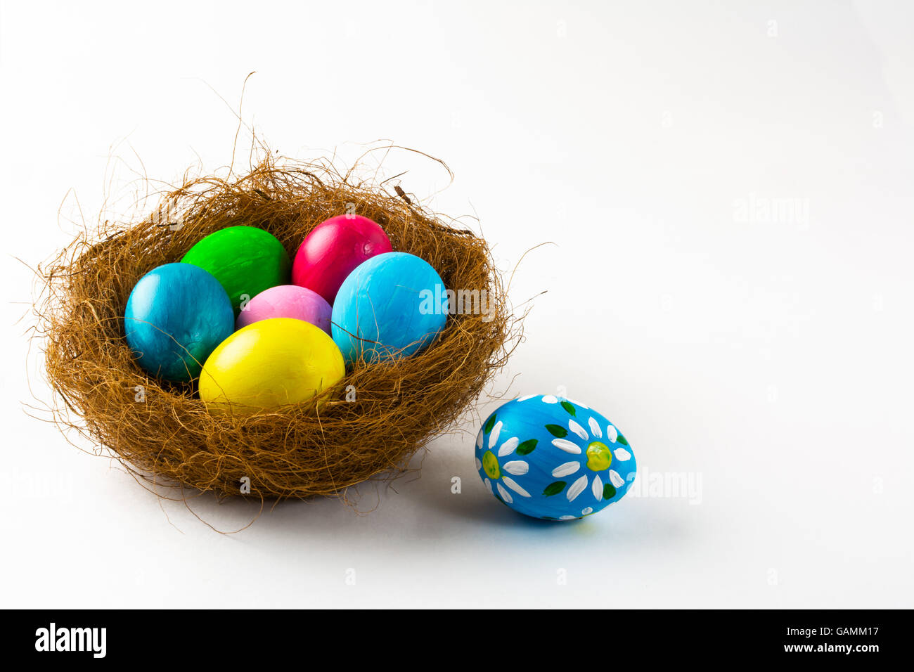 Bunte Ostereier in einem Nest und blauen Osterei mit Blumenmuster auf weißem Hintergrund. Ostern-Hintergrund. Symbol für Ostern. Stockfoto