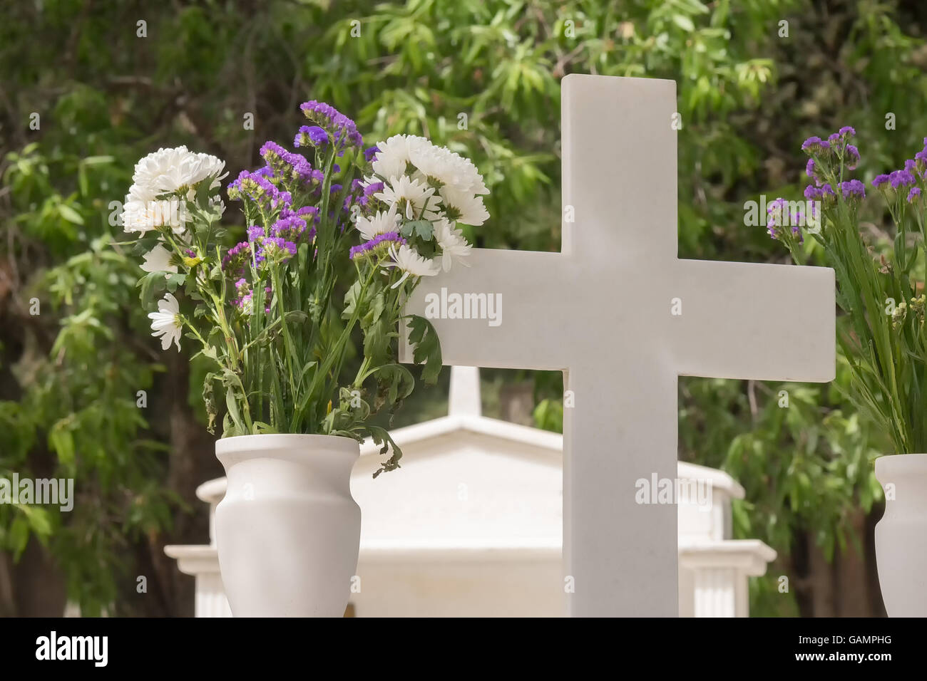 Christliches Kreuz auf einem Grab mit einer Blume daneben. Stockfoto