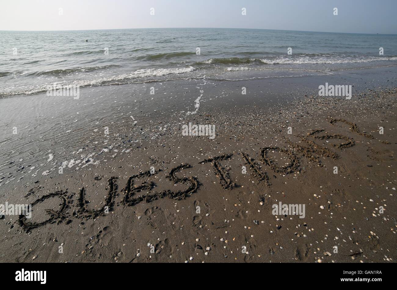 Fragen mit Fragezeichen geschrieben in großen Lettern auf dem Sand des Meeres im Sommer Stockfoto