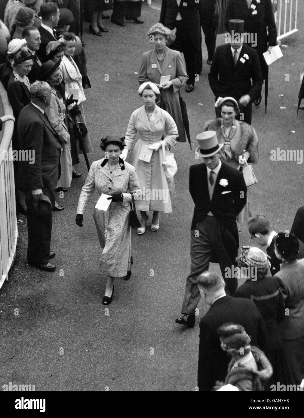 Racegoers beugen sich vor der Königin und Mitgliedern der königlichen Familie, die beim Royal Ascot Race Meeting im Fahrerlager zu Fuß zu sehen sind. Stockfoto