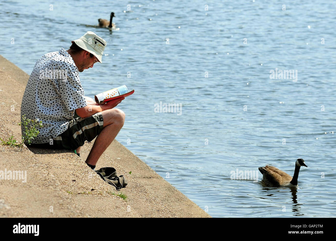 Ein Mann genießt das warme Wetter, als er am Ufer des Trent in der Nähe der Trent Bridge in Nottingham liest. Stockfoto