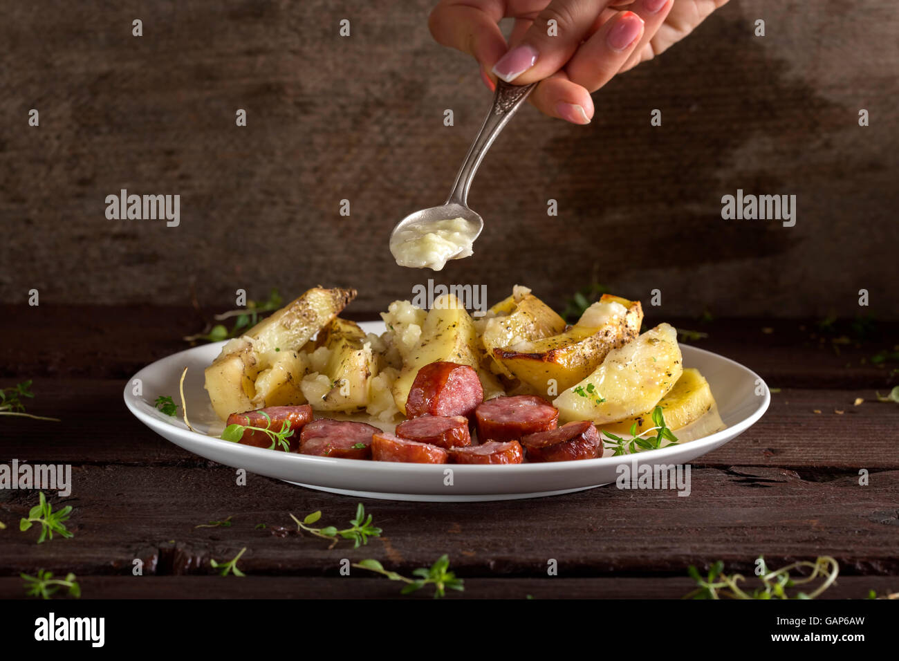 Hand, Knoblauch-Sauce über Bratkartoffeln mit Würstchen und Gewürzen über hölzerne Hintergrund Stockfoto