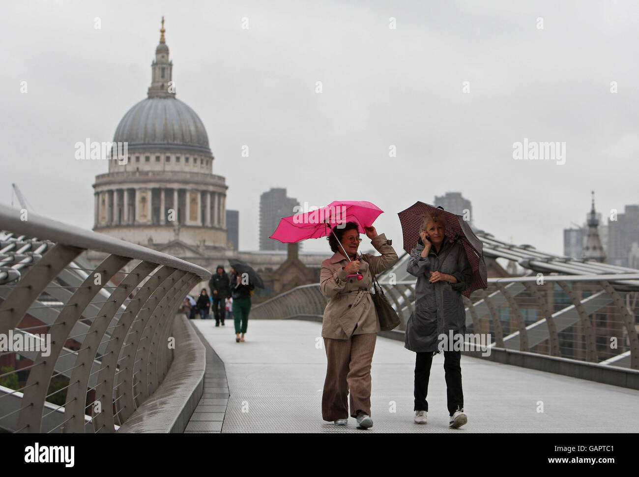 Die Menschen kämpfen durch starke Winde und Regen, wenn sie die Millennium Bridge in London überqueren. Stockfoto