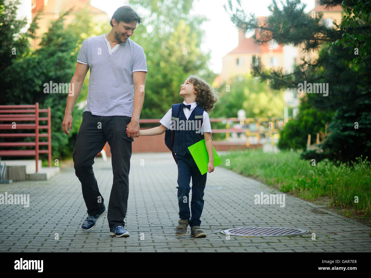 Dad es unter einem Erstklässler zur Schule. Er hält die Hand seines Sohnes. Kleine Schüler ist elegant gekleidet. Hinter dem jungen Rucksack. Stockfoto