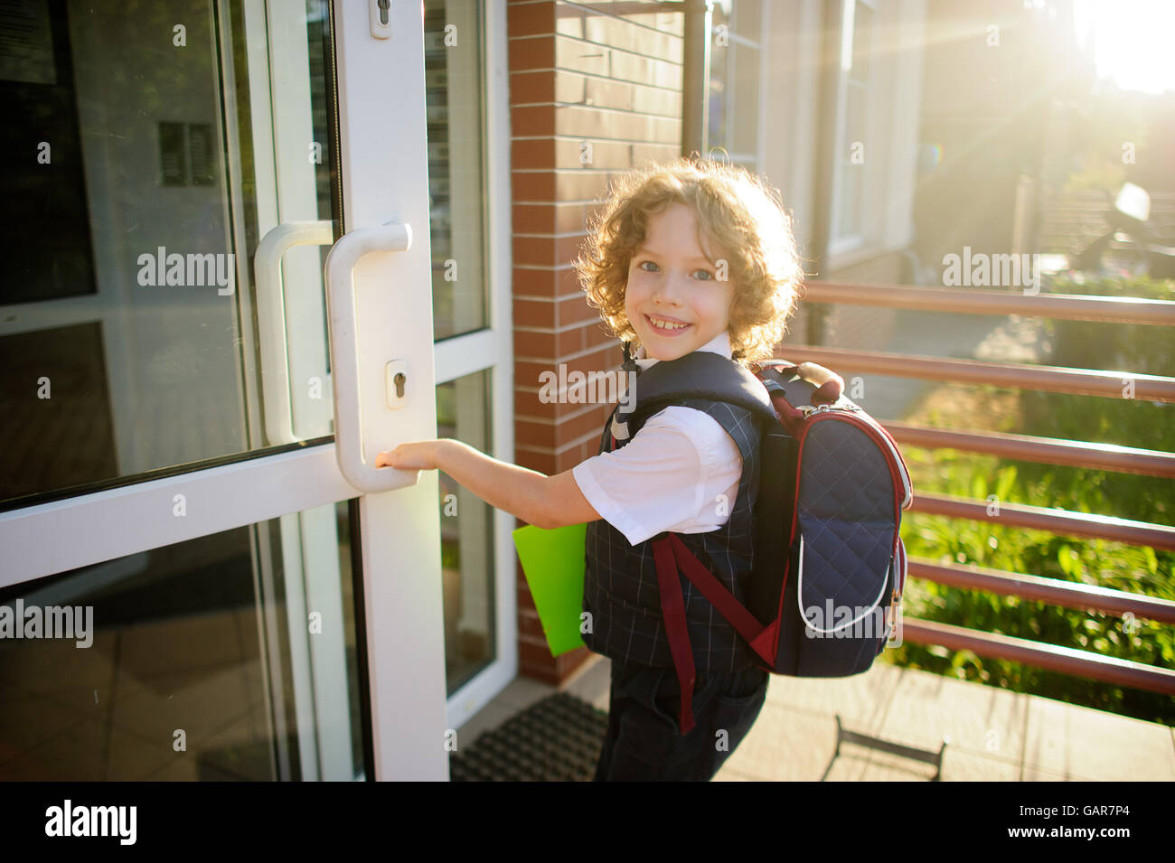 Kleine versaute Schüler eröffnet einer Schule. Der junge hübsches Gesicht. Hinter den Rucksack, in den Händen der hellen grünen Ordner. Sch Stockfoto