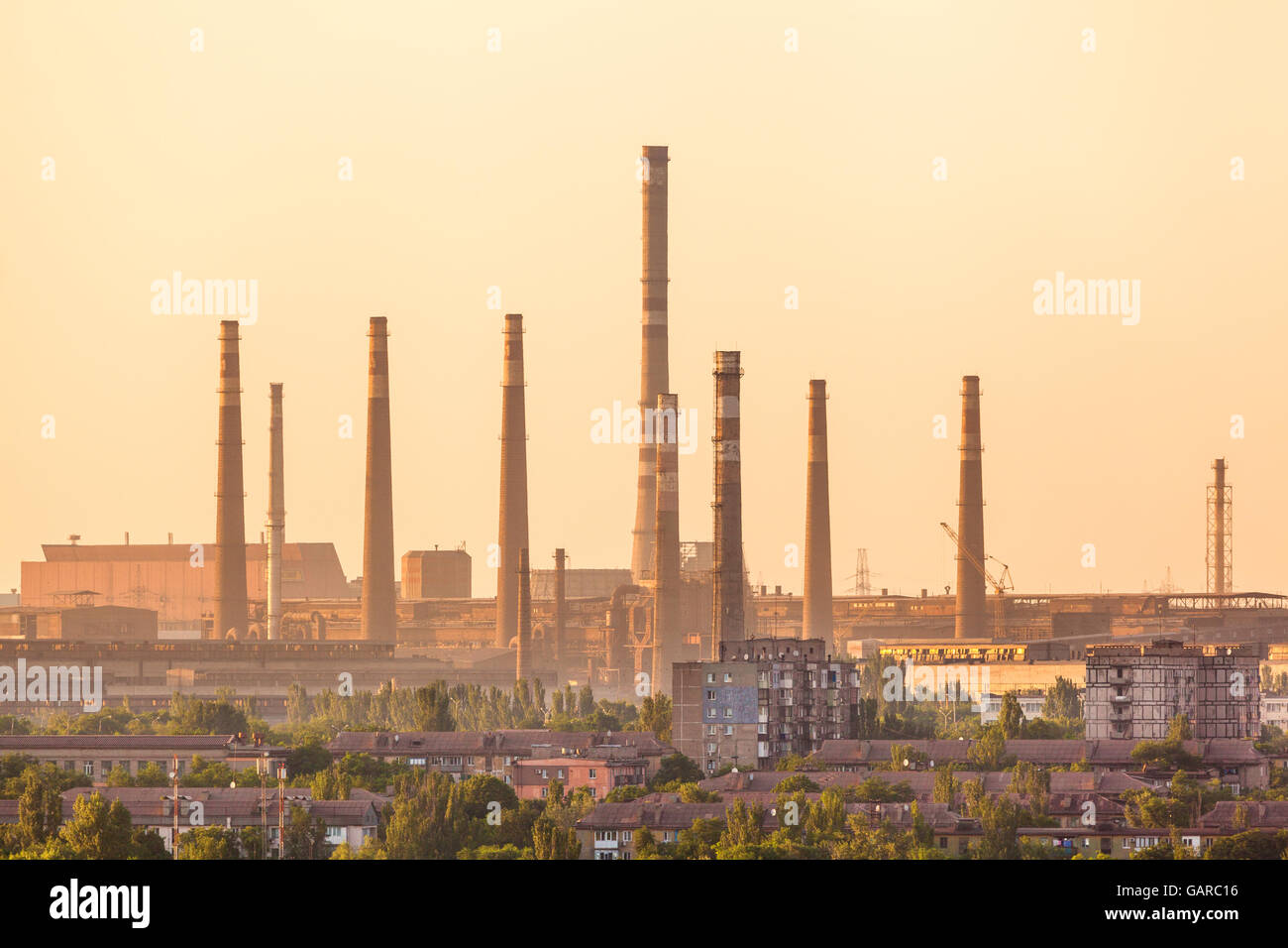 Gebäude der Stadt auf dem Hintergrund der Stahlfabrik mit Schornsteinen an farbenprächtigen Sonnenuntergang. metallurgische Fabrik. Stahlwerke, Eisen wor Stockfoto