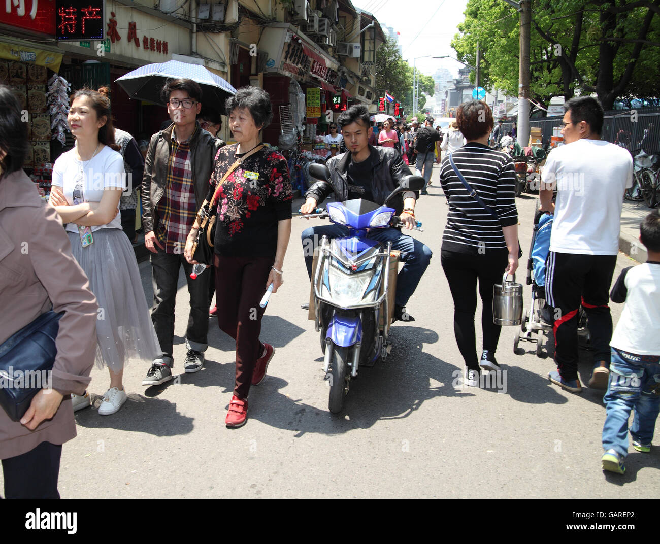 Ein chinesischer Mann reitet auf seinem Roller, rangieren in der Masse zwischen Fußgängern eine typische chinesische Straßenszene. Shanghai, China. 30.04.2016. Stockfoto