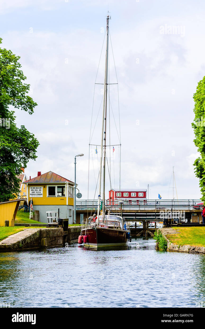 Motala, Schweden - 21. Juni 2016: Braun Segelboot durch die Schleuse fahren mit Brücke im Hintergrund. Echte Menschen in alltäglichen l Stockfoto