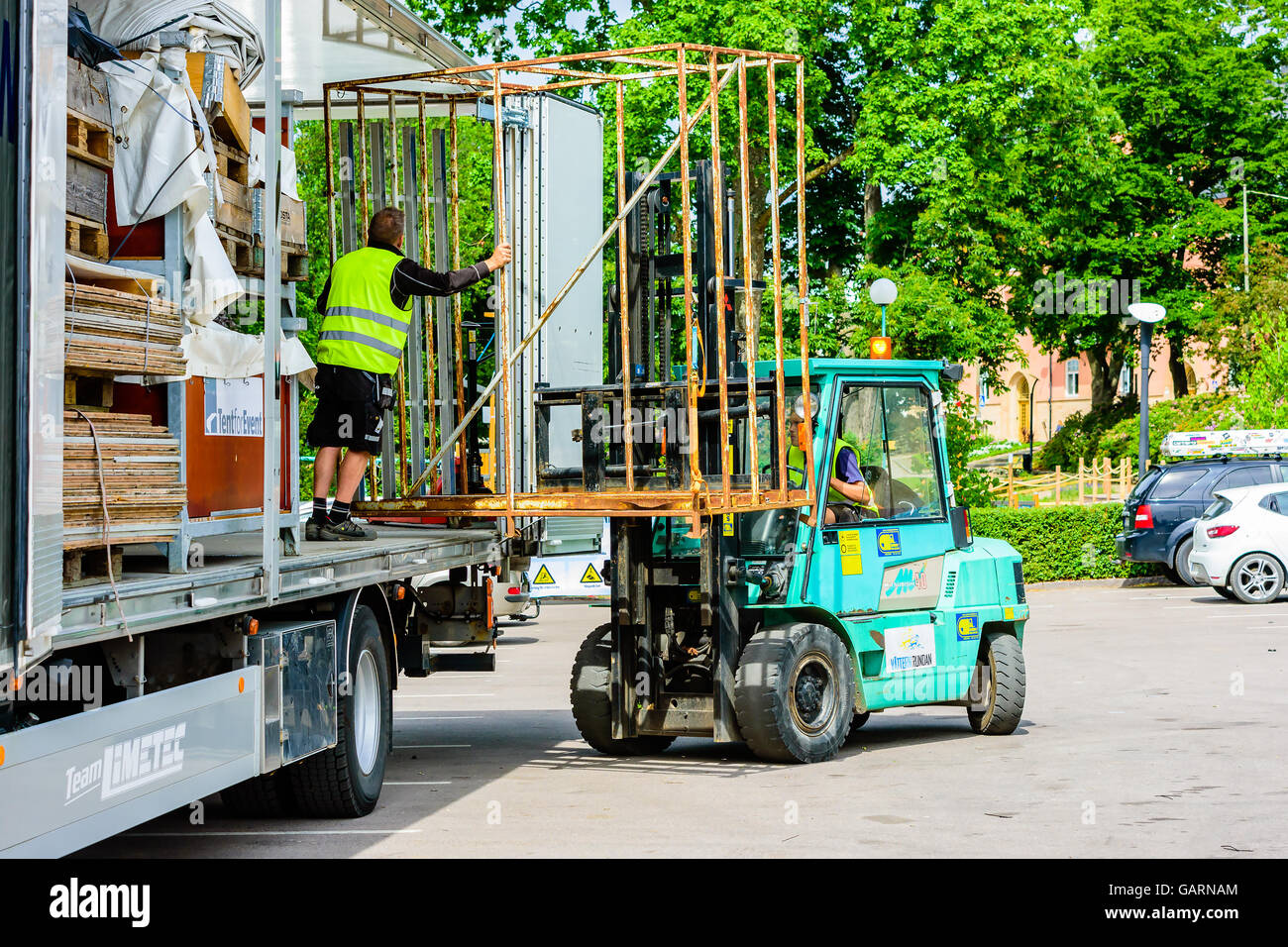 Motala, Schweden - 21. Juni 2016: Arbeiter laden oder ein Steel Cage von der Rückseite eines Lkw entladen mit einem kleinen Gabelstapler. Real Life sitzen Stockfoto