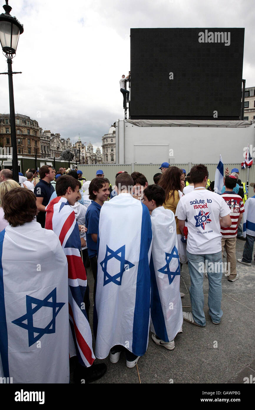 Die Massen schauen nach, wie ein pro-palästinensischer Demonstrator den mobilen Fernsehbildschirm skaliert, um während der Salute to Israel Parade auf dem Trafalgar Square, London, Großbritannien, zu demonstrieren. Stockfoto