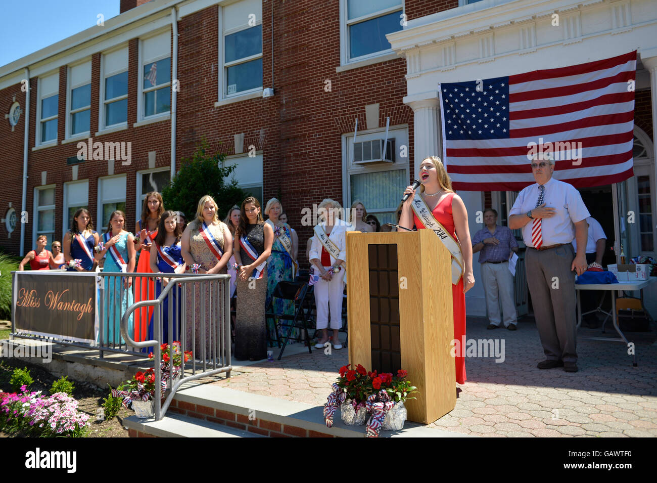 Wantagh, New York, USA. 4. Juli 2016.  KAYLA KNIGHT, Miss Wantagh 2014 singt God Bless America mit Hon. CHRISTOPHER QUINN stehend nach rechts von ihr und Krawatte rot weiß und blau, zum Jahresbeginn die bei der 60. jährliche Miss Wantagh Festzug, eine Tradition der Unabhängigkeitstag auf Long Island. Richter Christopher Quinn ist der Nassau County Überwachung Richter des Amtsgericht und handeln Richter am Obersten Gerichtshof. Bildnachweis: Ann E Parry/Alamy Live-Nachrichten Stockfoto