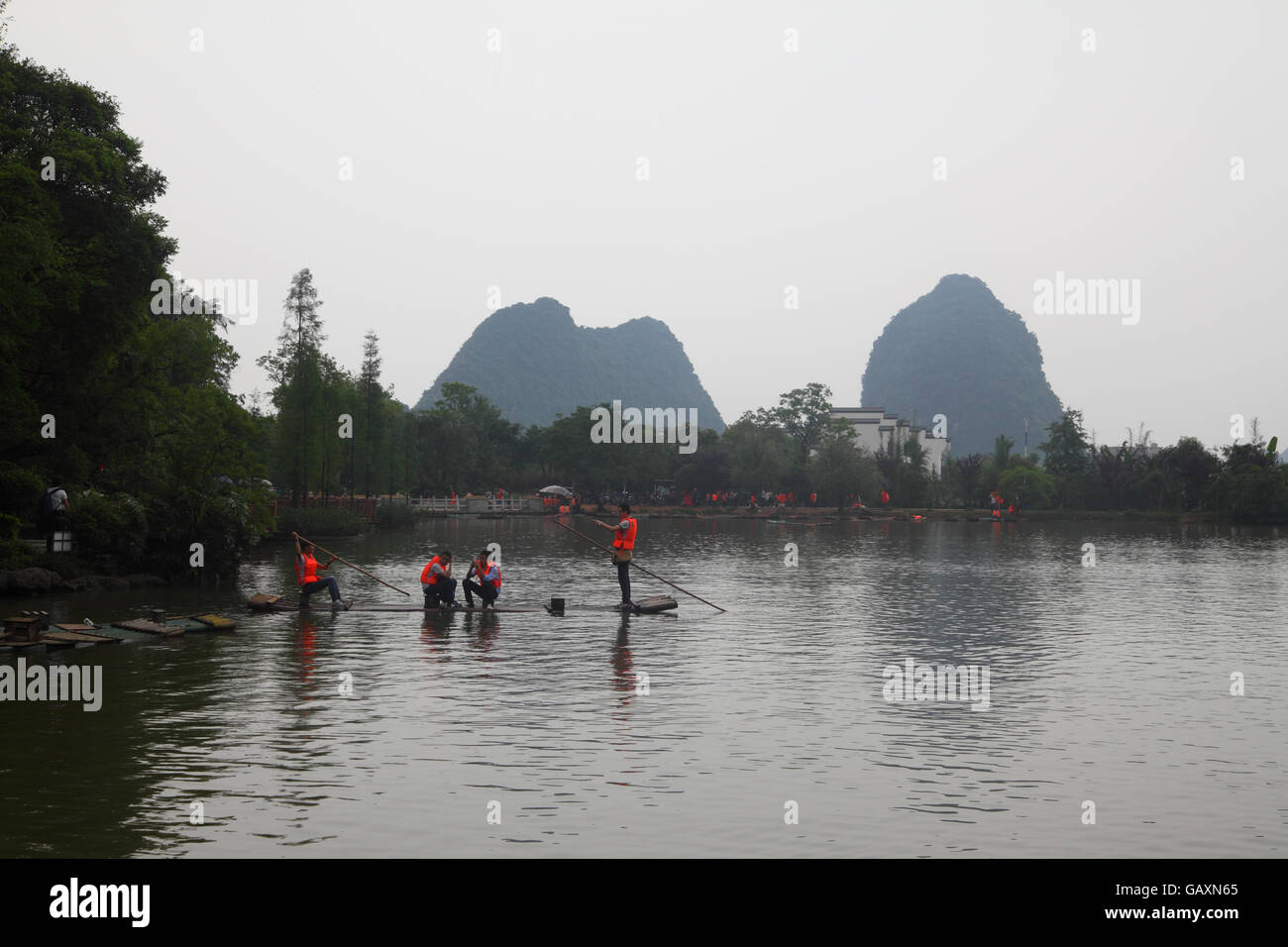 Menschen Rudern einen schmalen Floß auf Spring Lake, sind andere Boote und Karst Hügeln im Hintergrund zu sehen. Einem bewölkten Tag in Guilin, Guangxi, China. Stockfoto