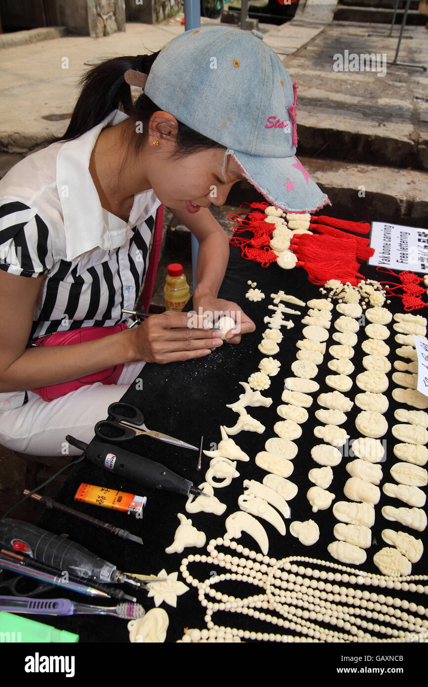 Eine chinesische Handwerkerin schnitzt Artefakte im Yak Knochen für Touristen als Souvenirs zu kaufen. Das Dorf Fu Li Li Fluss, Guangxi, China. Stockfoto