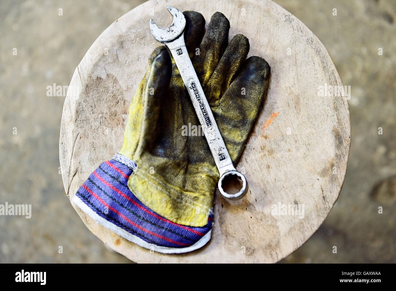 Schmutzige Arbeitnehmers Handschuh ein Schraubenschlüssel-Taste auf ein Holzbrett in eine Werkstatt Stockfoto