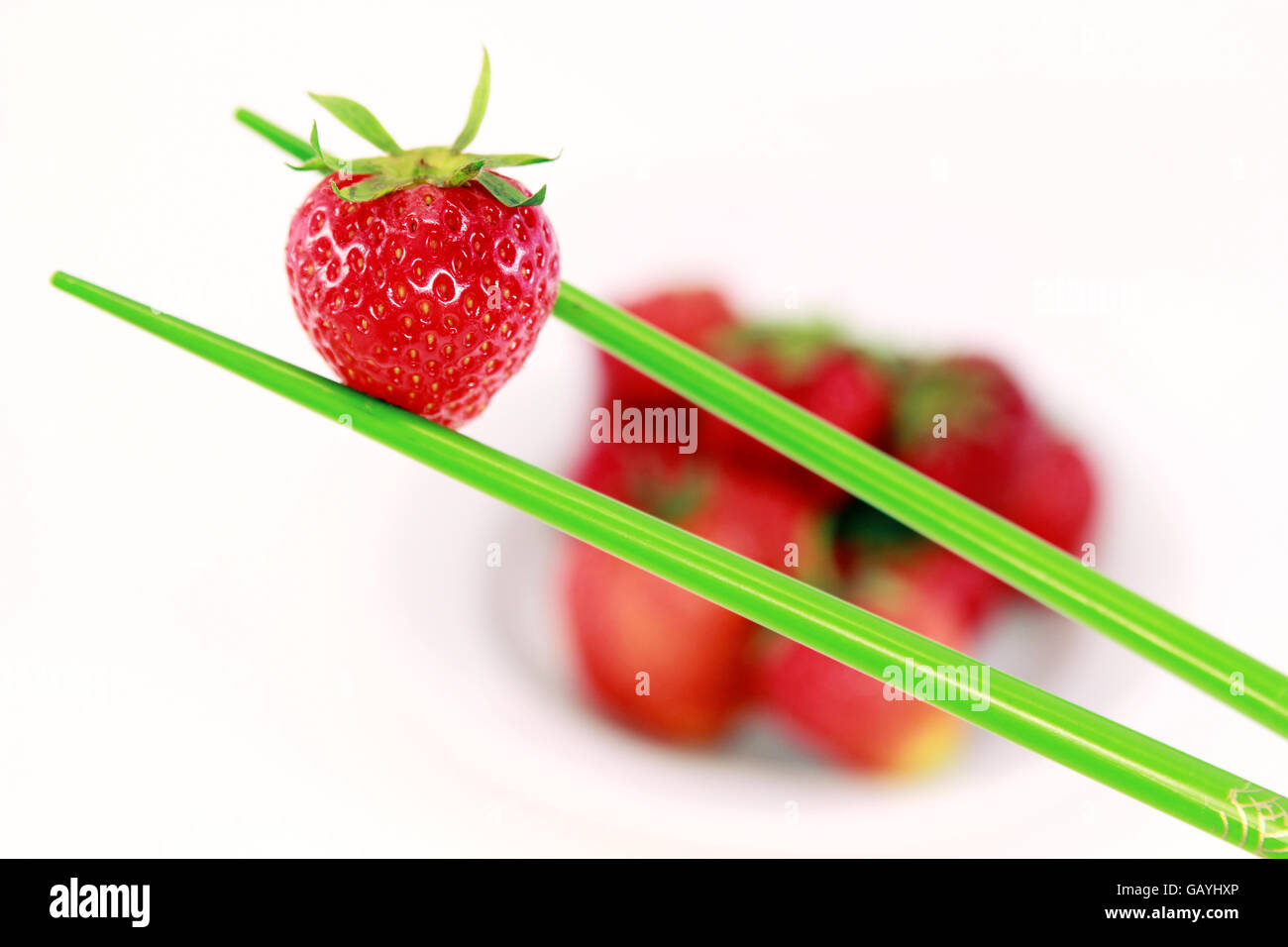 rote Erdbeere halten mit grünen Stäbchen in Nahaufnahme weißen Hintergrund Stockfoto