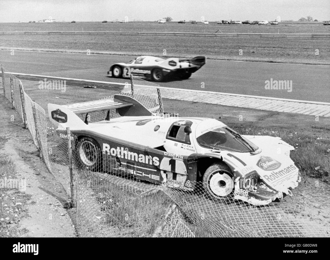 Der Derek Bell/Stefan Bellof Rothmans Porsche rast auf dem Weg zum Sieg in den 1.000 km Silverstone an ihren abgestürzten Teamkollegen Jacky Ickx/Jochen Mass vorbei. Stockfoto