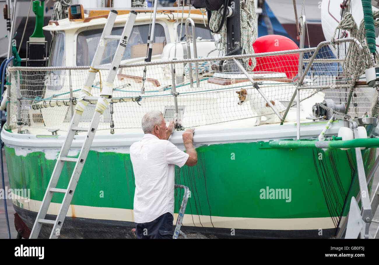 Älterer Mann Reparatur Yacht während Hund ihn vom Deck in Werft in Las Palmas auf Gran Canaria, Kanarische Inseln, Spanien beobachtet Stockfoto