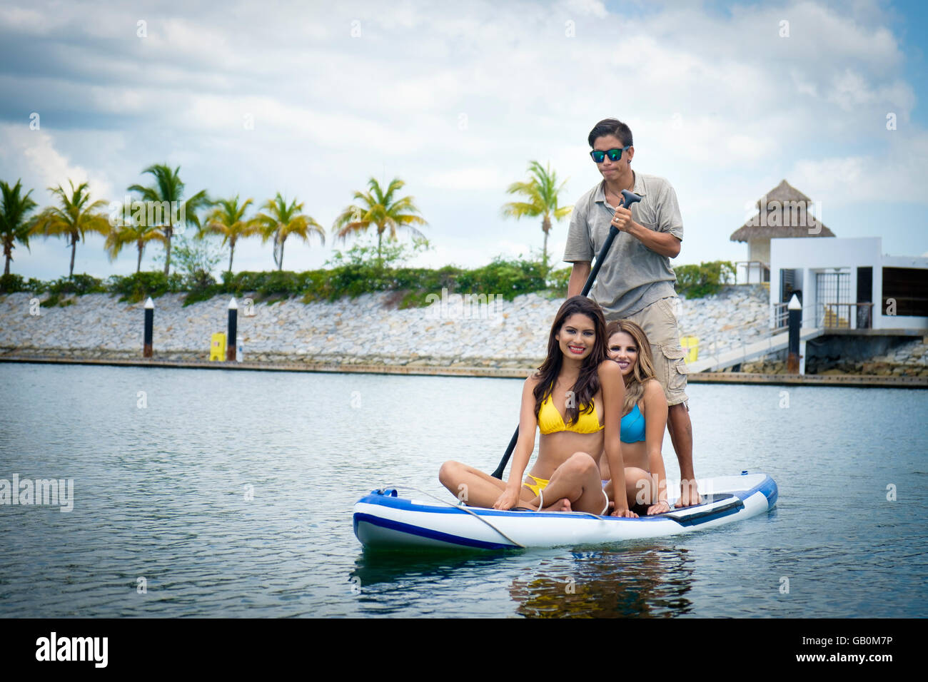 2 junge Frauen und ein Mann reitet auf einem Paddle Board in einer Marina in Mexiko. Stockfoto