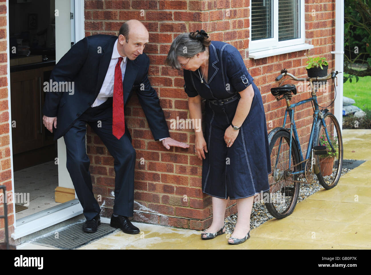 Hochwasserrückgewinnung Minister John Healey hält seine Hand gegen die Wand und zeigt den Wasserstand an, der das Haus von Frau Jane Aston (links) während der Überschwemmungen im letzten Jahr in Tewkesbury überflutete. Stockfoto