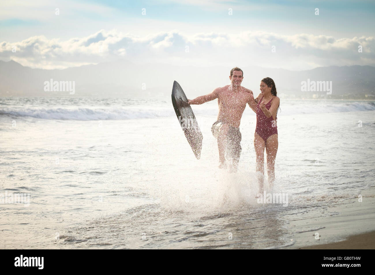 Junges Paar am Strand mit Boogie Board, Spritzwasser läuft. Riviera Nayarit, Mexiko. Stockfoto