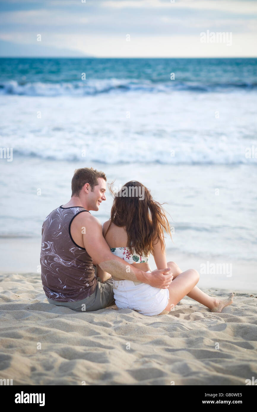 Rückseite des jungen Paares in ihren 20ern sitzen am Strand Stockfoto