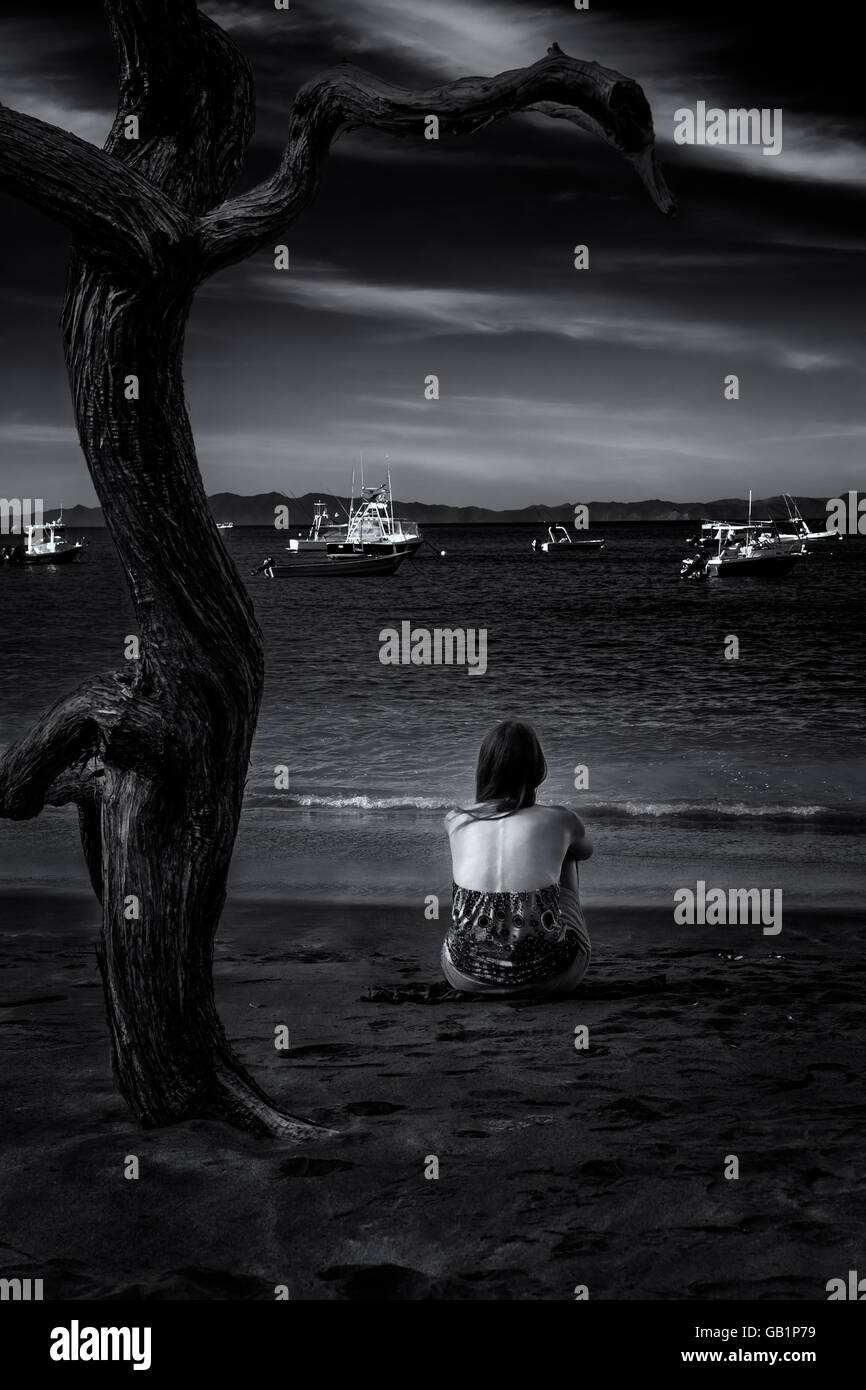 Schöne Frau sitzt alleine auf Ocotal Beach und mit Blick auf Boote vor Anker in der Bucht, Guanacaste, Costa Rica Stockfoto Schöne Frau sitzt alleine auf Ocotal Beach und mit Blick auf Boote vor Anker in der Bucht, Guanacaste, Costa Rica Stockfoto