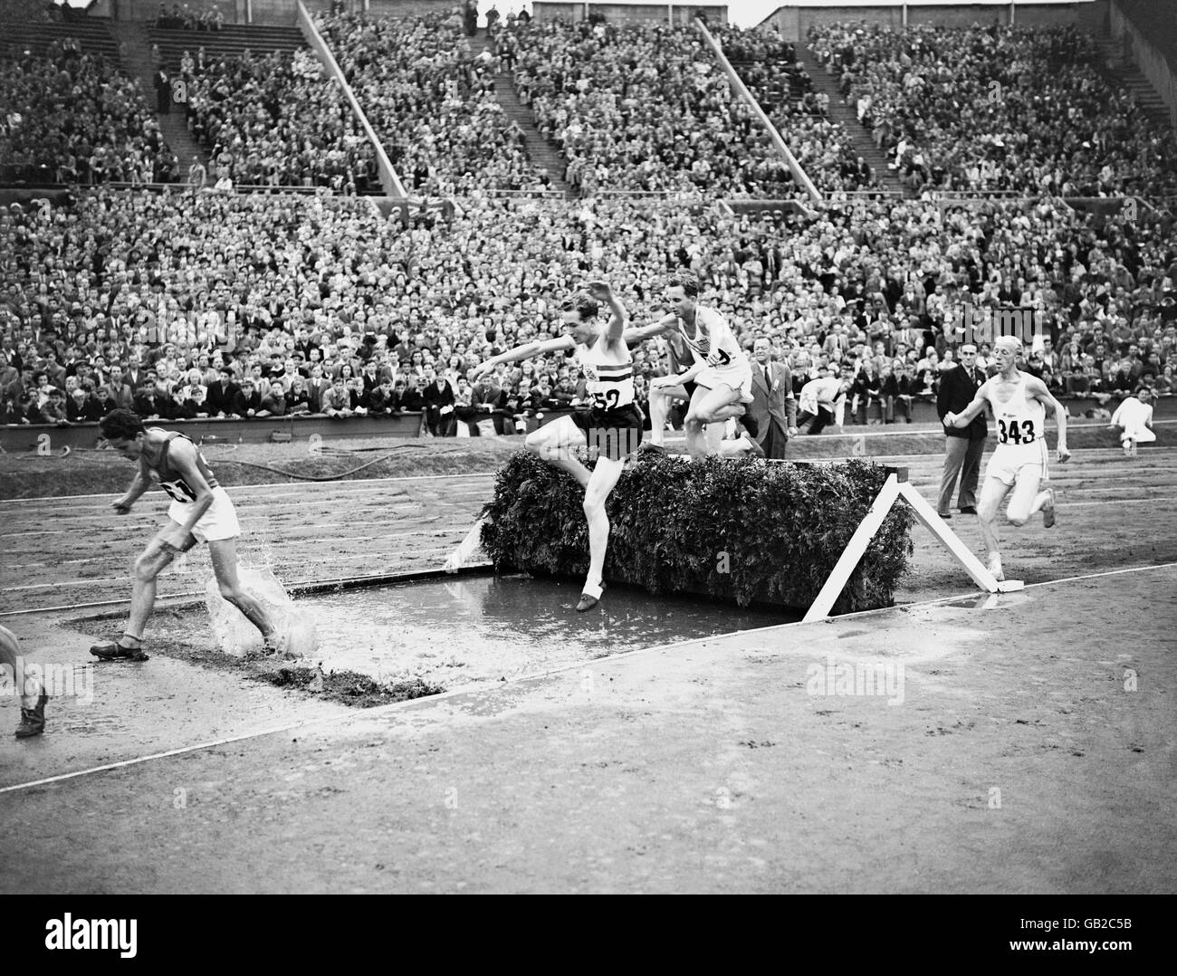 Olympische Spiele 1948 In London - Leichtathletik - Steeplechase - Wembley. Teilnehmer, die während eines der Heats der 3000 m langen Steeplechase der Männer über einen der Wassersprünge fahren. Stockfoto