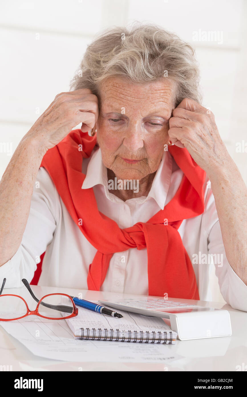 Finanzielle Probleme. Frustriert senior Frau lehnte ihren Kopf auf Seite beim Sitzen am Tisch mit Rechnungen und Rechner es Stockfoto