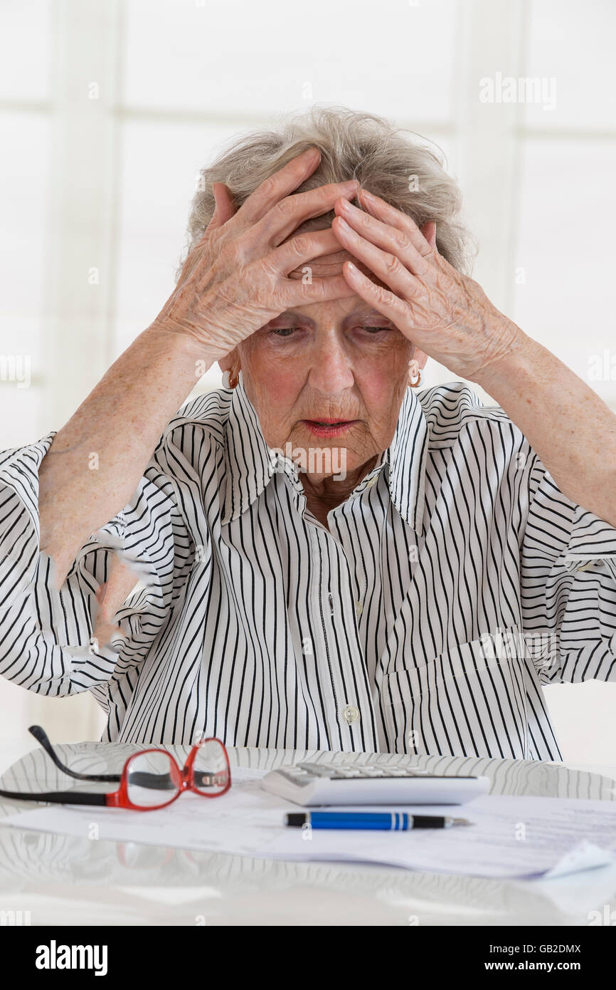 Finanzielle Probleme. Frustriert senior Frau lehnte ihren Kopf auf Seite beim Sitzen am Tisch mit Rechnungen und Rechner es Stockfoto