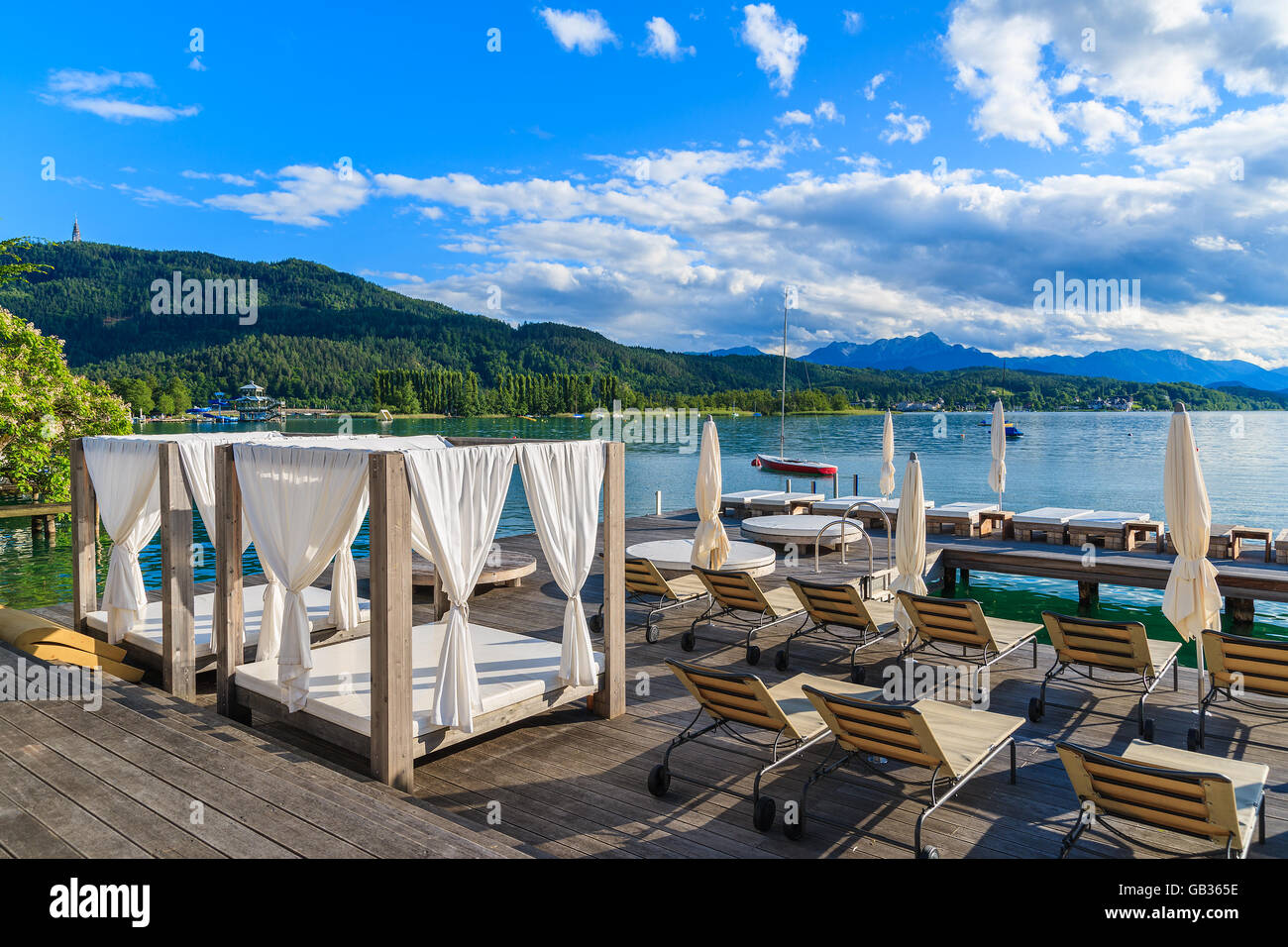 Liegestühle und liegen am Holzdeck und Blick auf den wunderschönen alpinen See Wörthersee im Sommer, Österreich Stockfoto