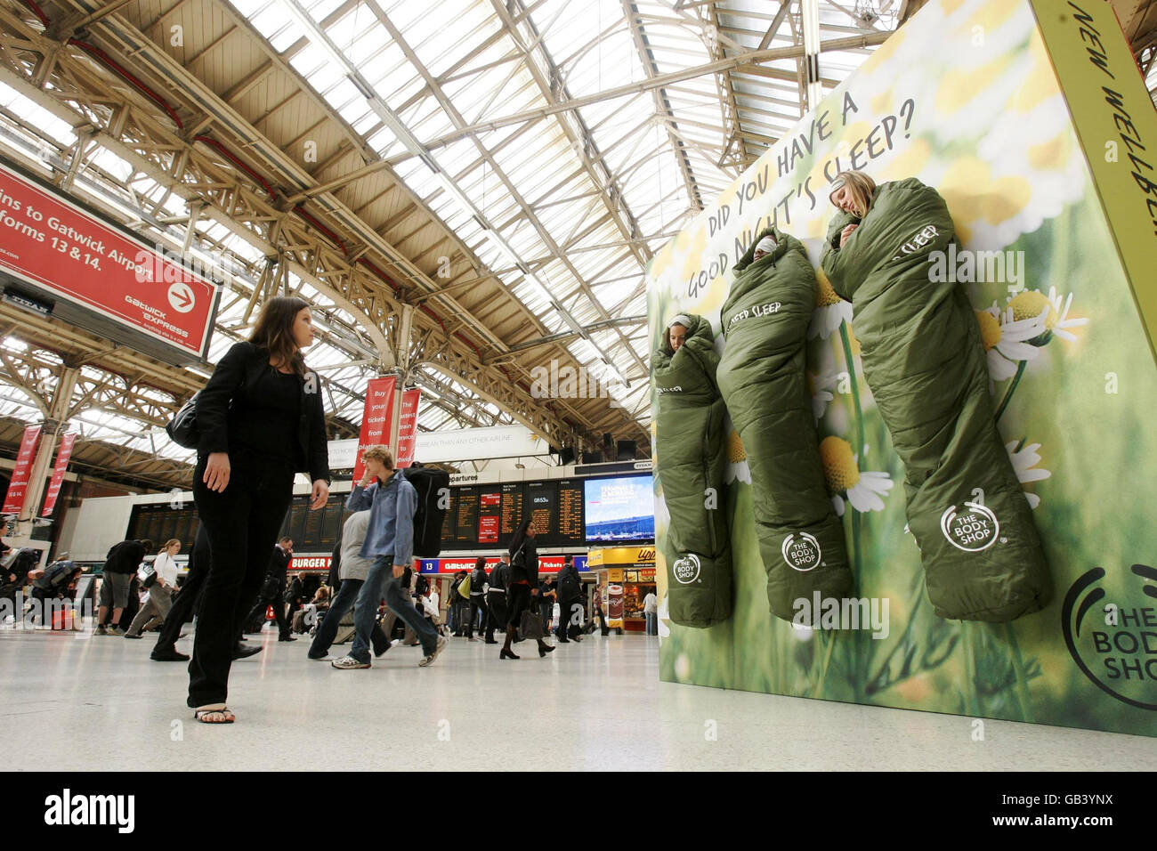 Drei Menschen fangen ihren Schlaf auf, als sie an einer Plakatwand in Victoria Station, London, hängen, um für die neue Wellbeing Deep Sleep Range von The Body Shop zu werben. Stockfoto
