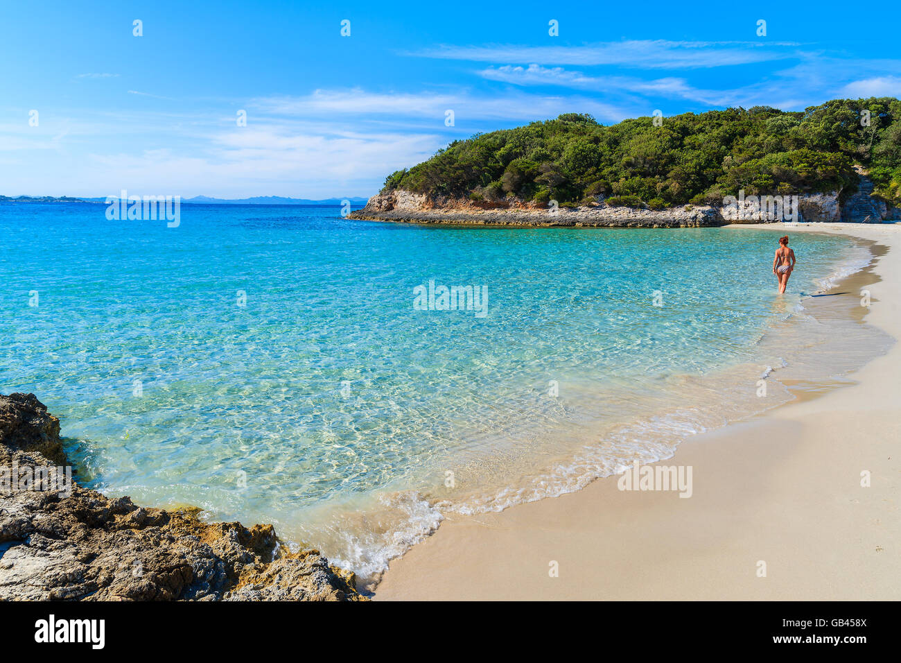 Unbekannte Frau zu Fuß entlang Petit Sperone Sandstrand mit azurblauen Meereswasser an der Küste von Korsika, Frankreich Stockfoto