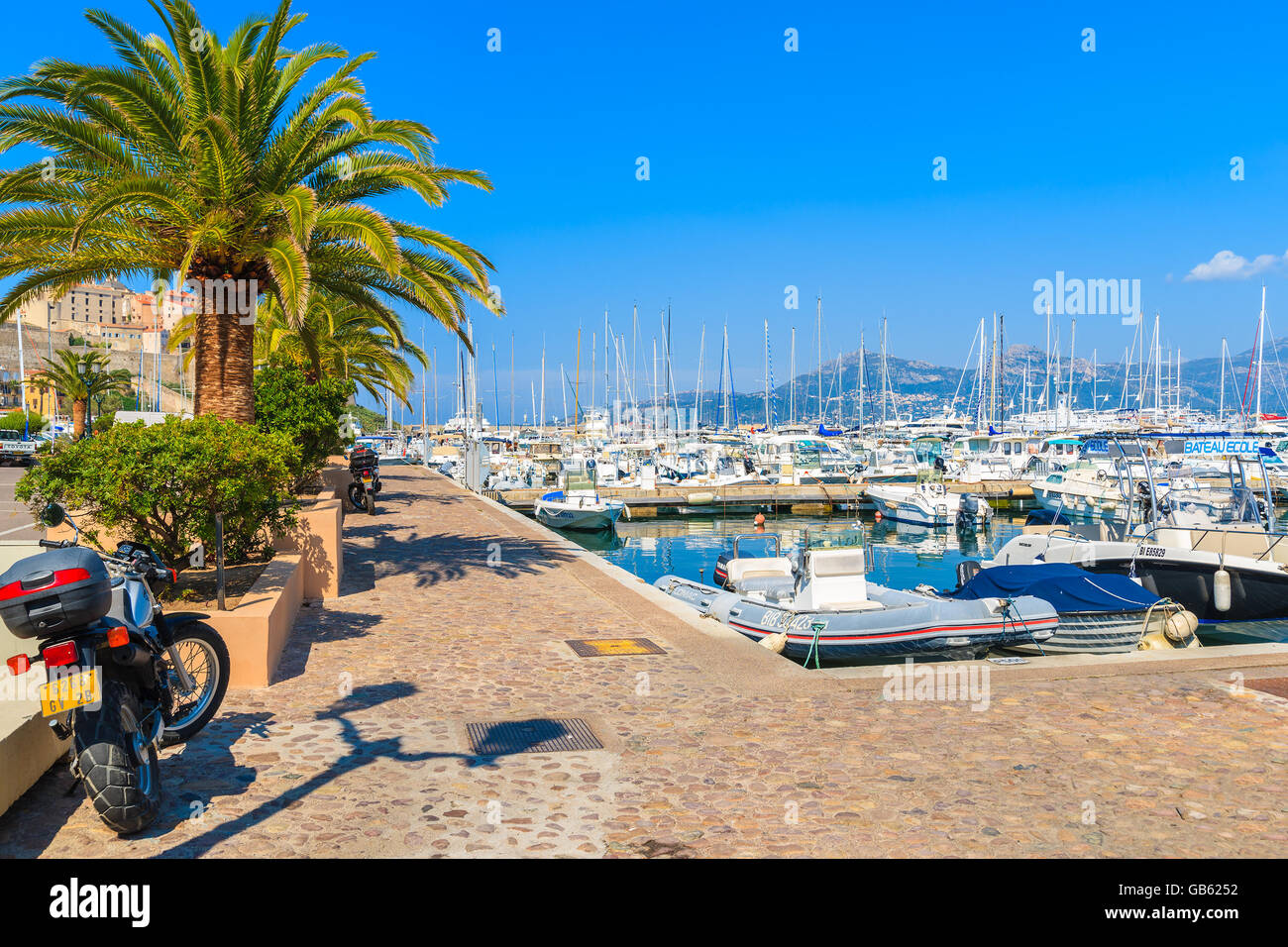 CALVI, Korsika - 28. Juni 2015: Scooter parkte auf der Strandpromenade mit Palmen im Hafen von Calvi. Diese Stadt hat luxuriöse Yachthafen Stockfoto