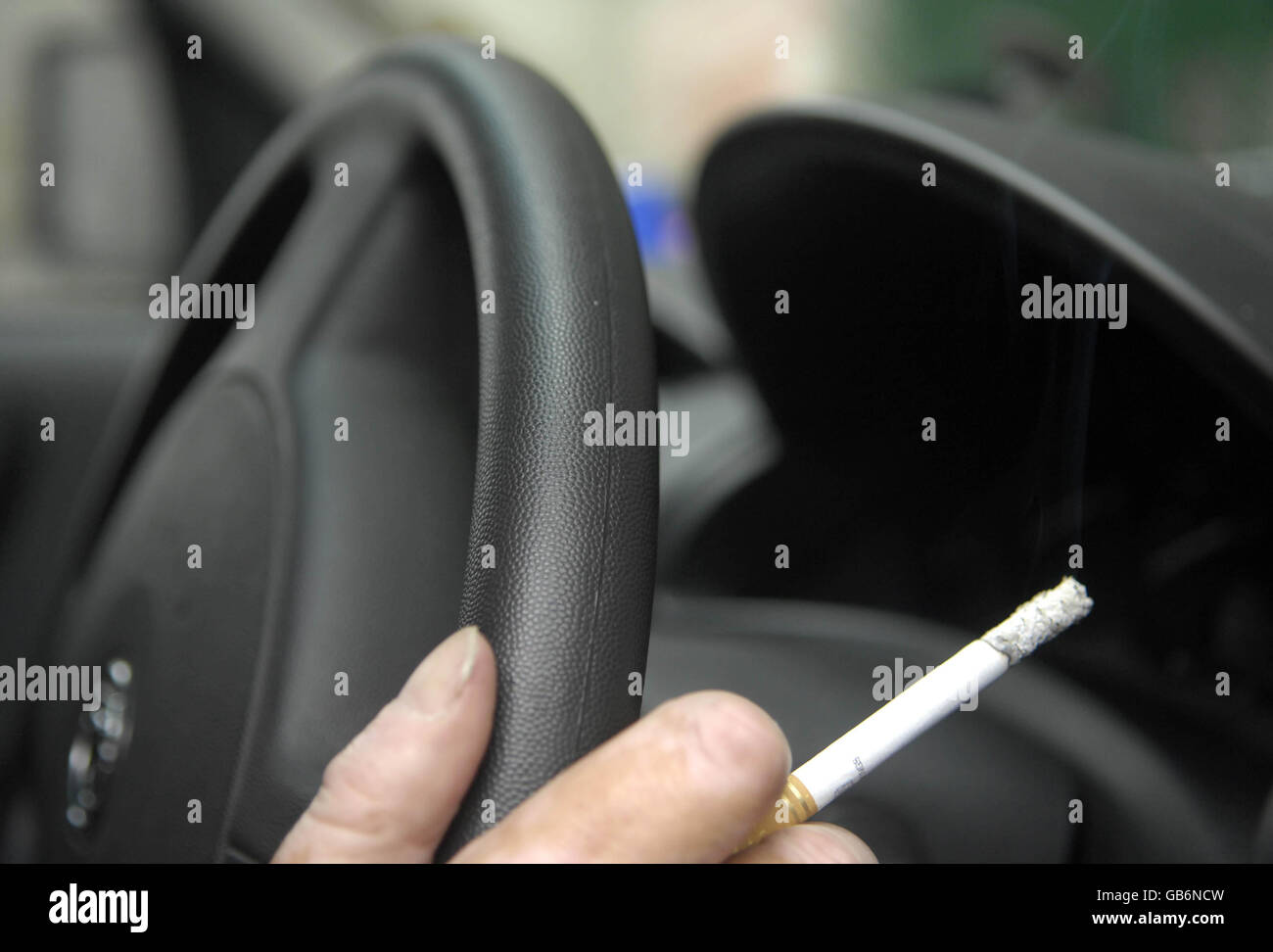 Ein Mann hält eine Zigarette, während er in London am Steuer eines Autos sitzt. Stockfoto
