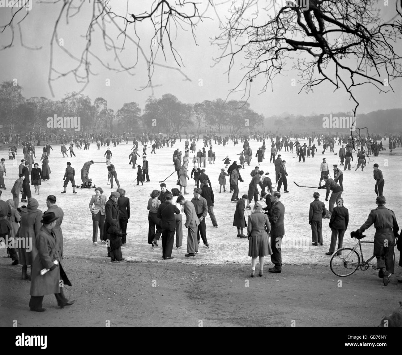 Menschen Eislaufen und Eishockey spielen auf dem gefrorenen Wimbledon Common Pond. Obwohl drei Menschen durch das Eis fielen, wurden die Skater nicht abgeschreckt. Stockfoto
