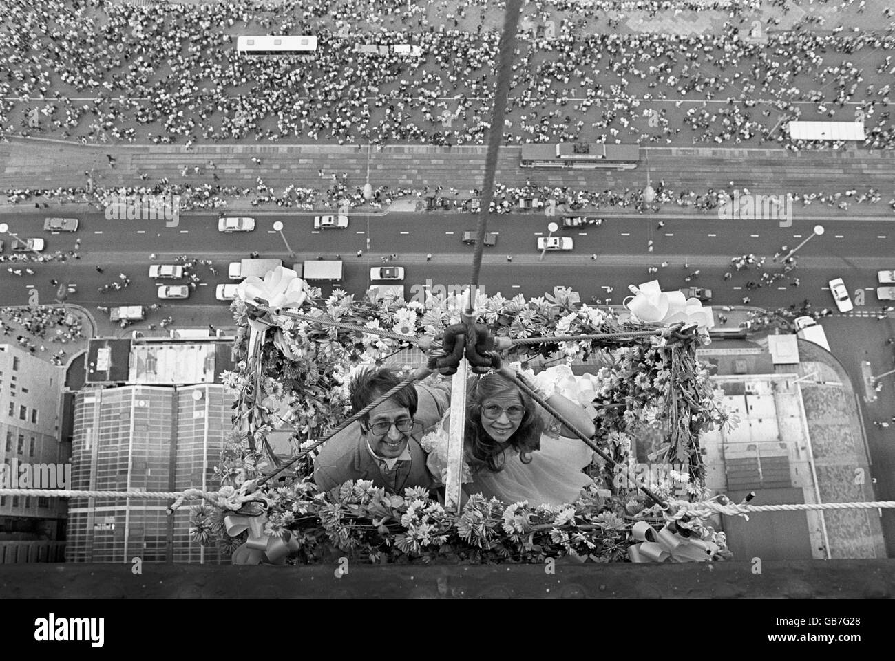 Der Eskapologe Karl Bartoni und seine Braut Wendy Stokes, die zum Segen ihrer bevorstehenden Hochzeit in Blumen gehäkelt waren, schweben am Blackpool Tower über einer Feriengemeinde auf der Promenade unten. Stockfoto