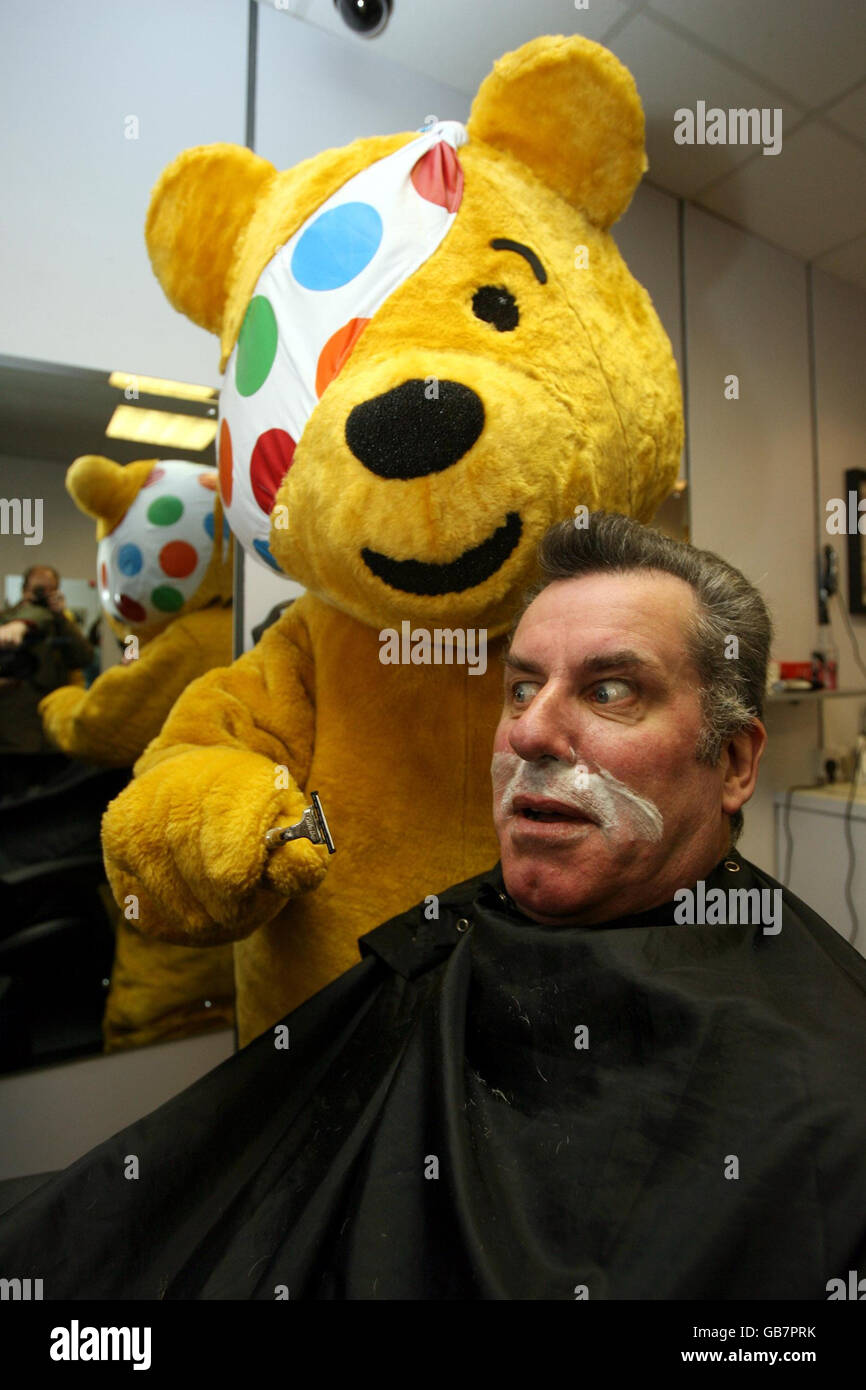 SDLP-Stadtrat Niall Kelly in der Kleidung von Pudsey Bear bereitet sich darauf vor, den typischen Schnurrbart des SDLP-Veteranen Alban Maginness for the Children in Need in seinem lokalen Friseurladen in Nord-Belfast abzurasieren. Stockfoto