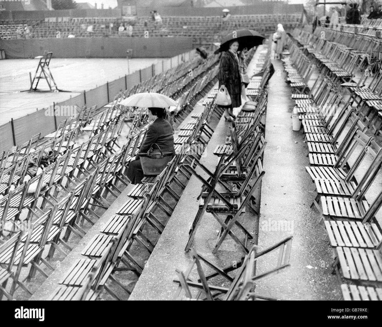 Ein paar Zuschauer mit Regenschirmen halten an und trotzen dem Regen, der bei den britischen Hartplatz-Tennismeisterschaften in Bournemouth nicht mehr gespielt hatte. Stockfoto