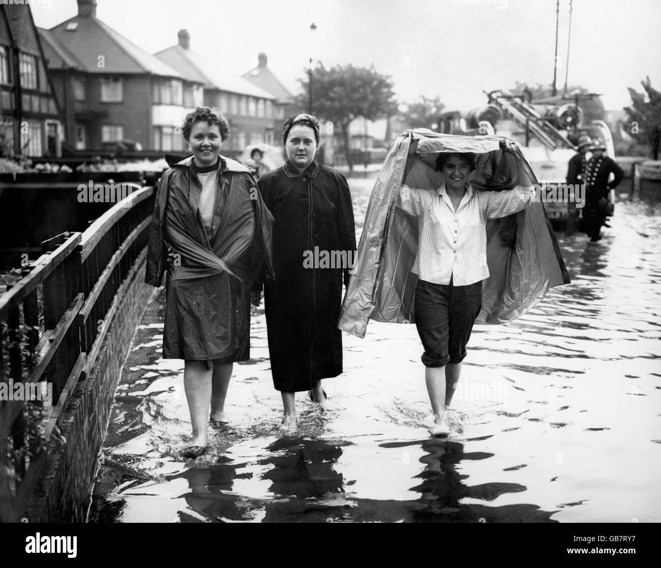 Drei Bewohner, von denen einer vor dem Regen schützt, gehen durch das Hochwasser in Waterbank Road, Catford, Südosten Londons. Stellenweise war das Hochwasser des geschwollenen Ravensbourne Flusses zehn Zentimeter tief. Stockfoto