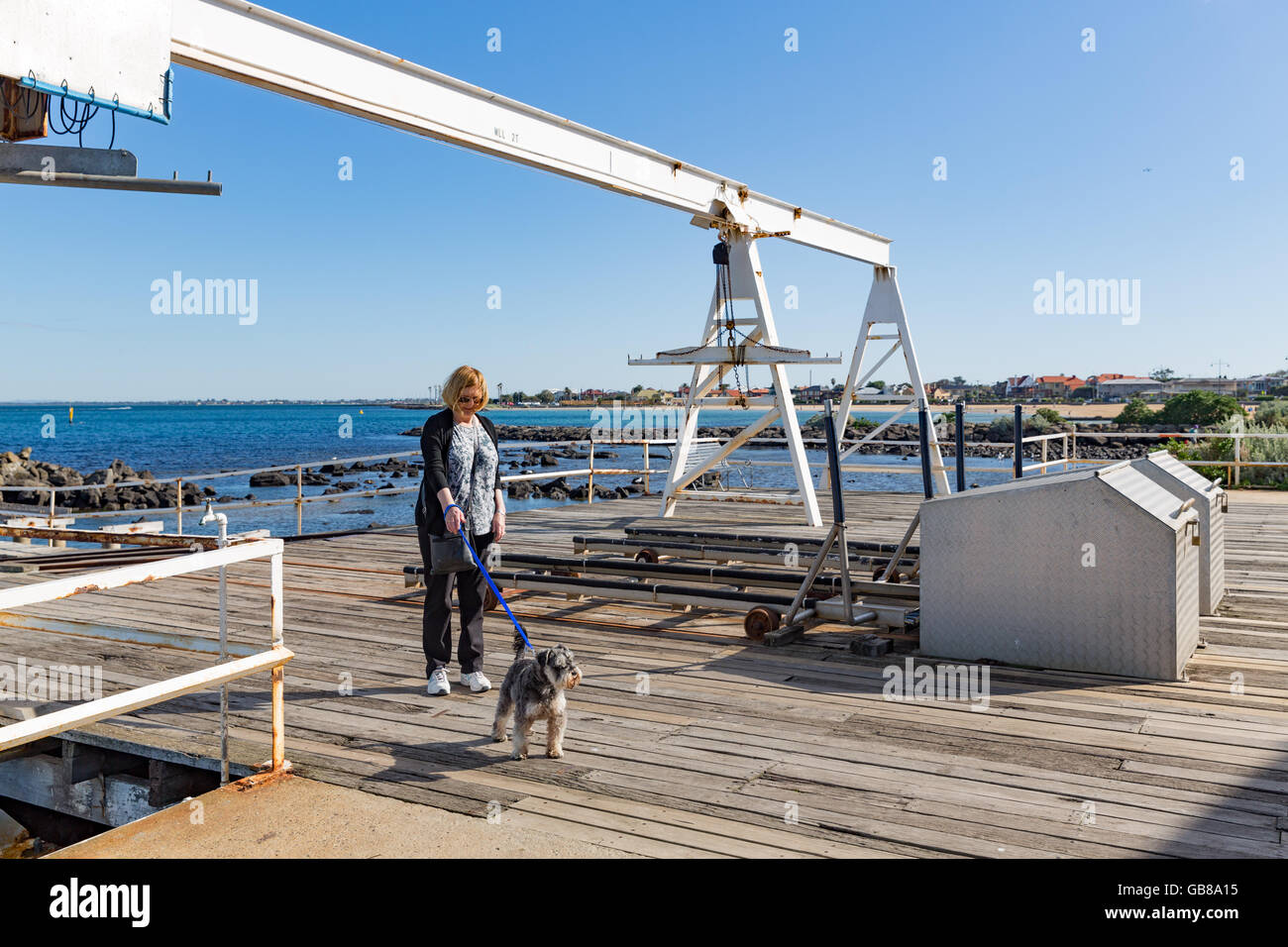 Eine Frau geht Hund unter Bootskran am Steg am Williamstown, Victoria, Australien Stockfoto